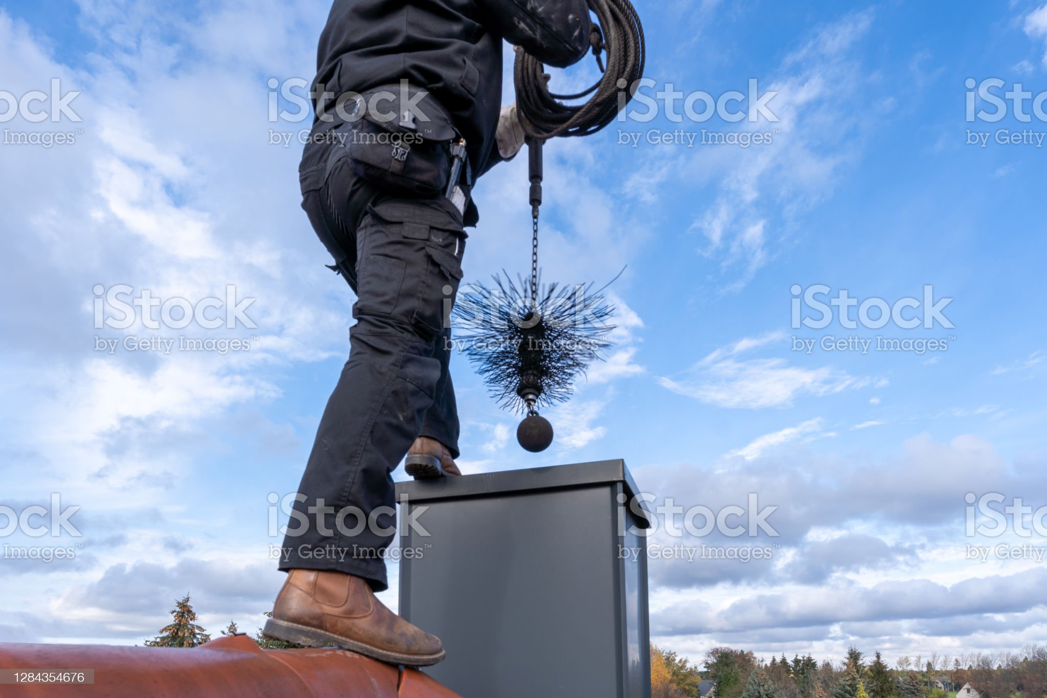 Chimney sweep cleaning a chimney standing on the house roof, lowering equipment down the flue